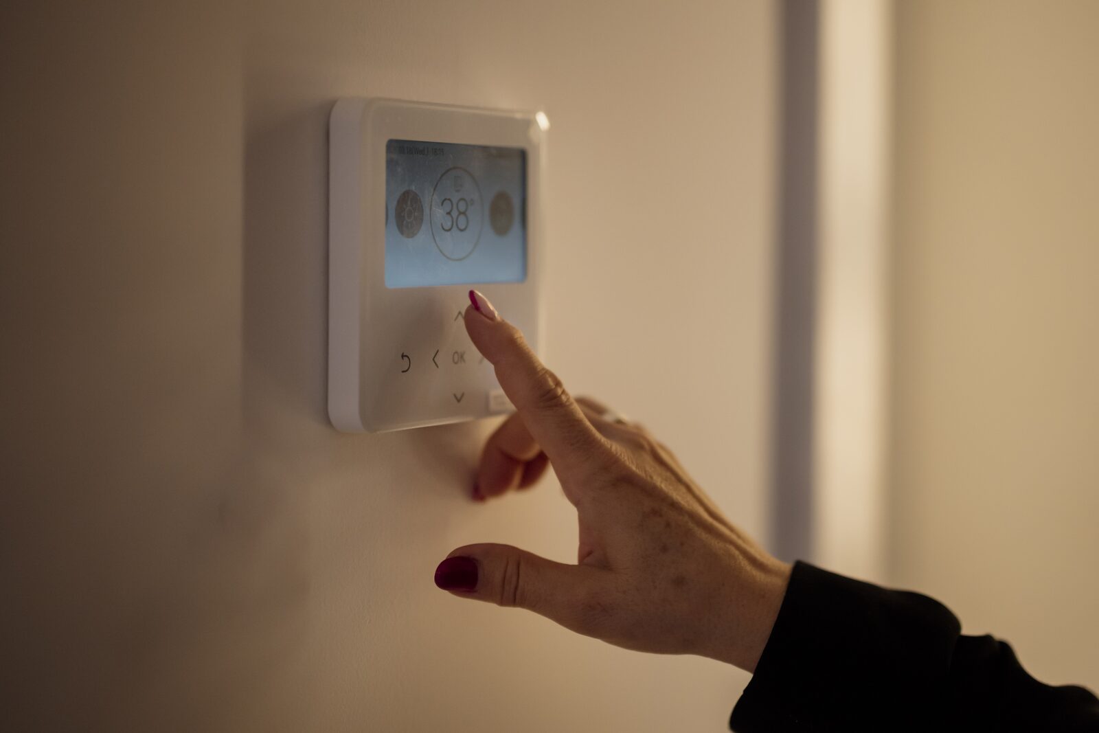 A hand adjusting a wall-mounted digital thermostat in a home