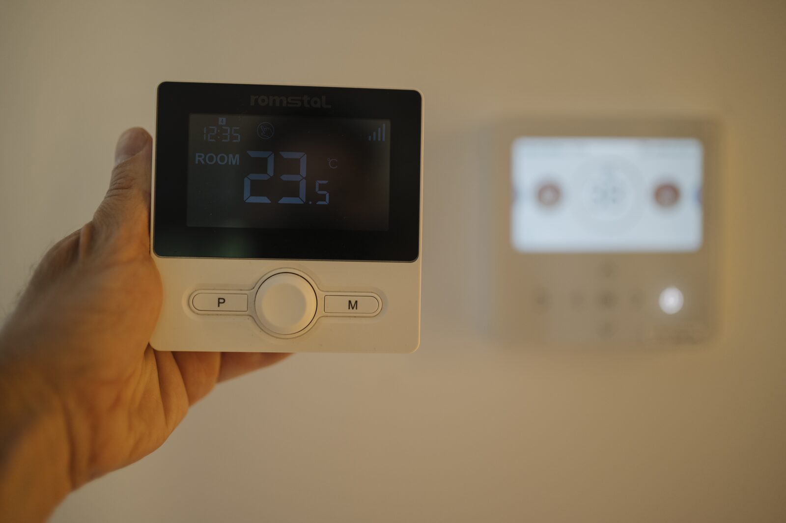 A person holding a digital thermostat in a home