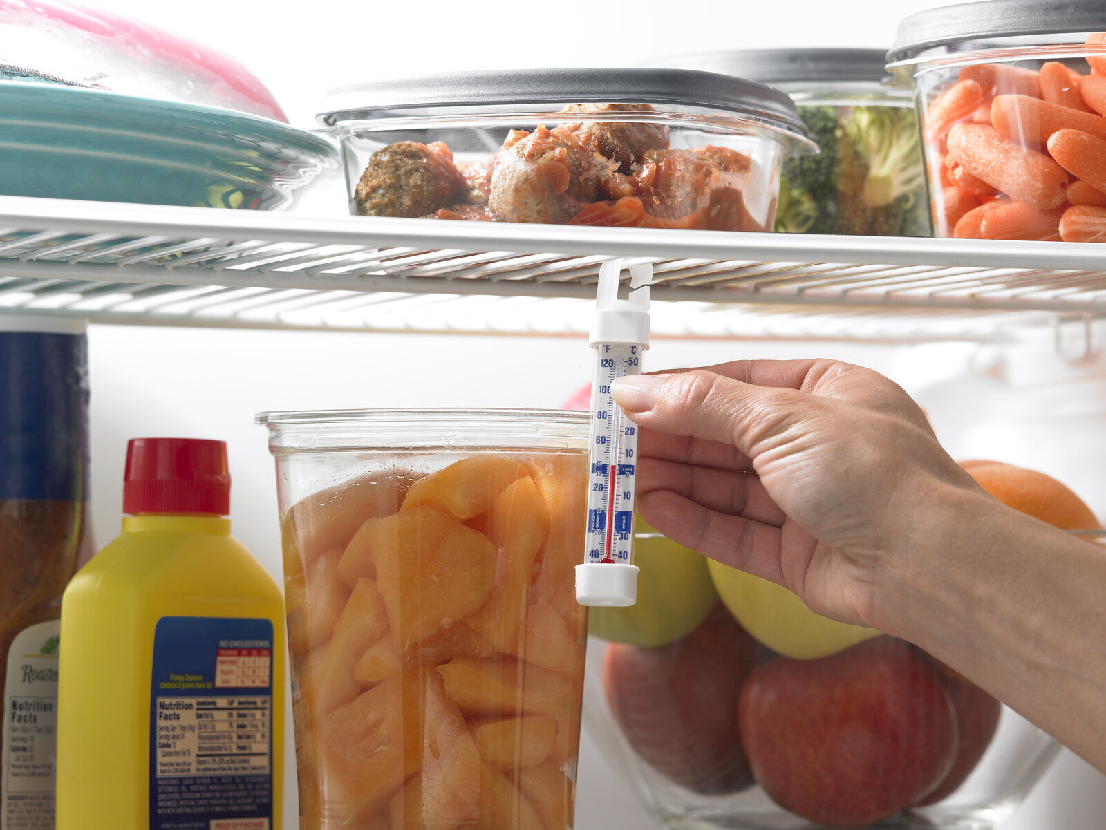 A hand reading a real appliance thermometer inside a refrigerator